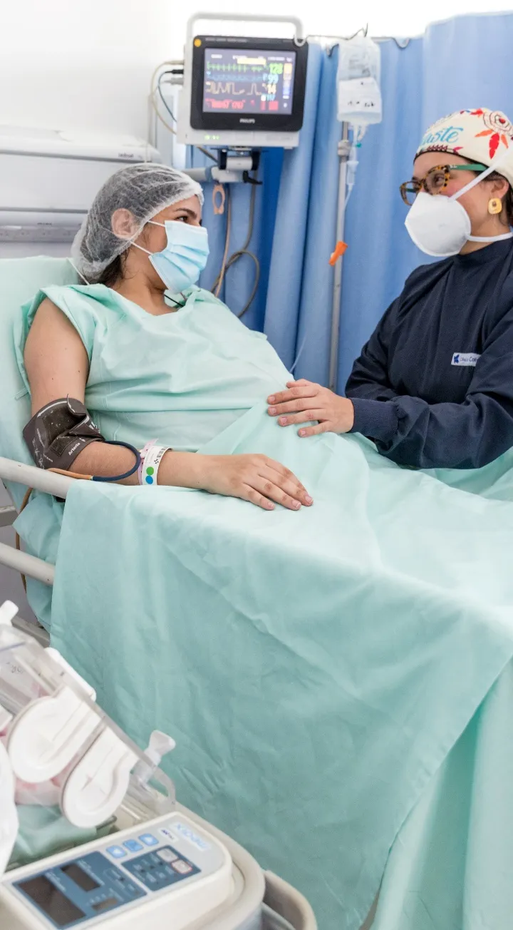En una camilla se ve a una mujer embarazada mirando a una profesional de la salud que tiene la mano sobre su vientre. 