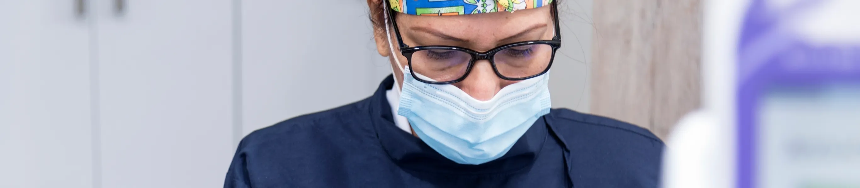 Hay una profesional de la salud que usa tapabocas, gorro quirúrgico y gafas mirando hacía abajo. 