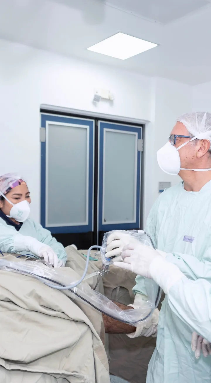 Hay dos profesionales de la salud manipulando instrumentos en lo que se puede inferir que es un procedimiento médico a un paciente. 